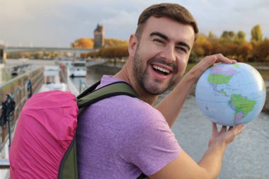 Gezgin çantalı yakışıklı bir gencin portresi. Nehirde küreyi tutuyor.