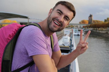 Sırt çantasıyla seyahat ederken barış jesti yapan yakışıklı bir gencin portresi