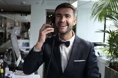 Smokinli genç bir adamın portresi. Papyonlu. Lüks bir iç mekanda telefonla konuşuyor.