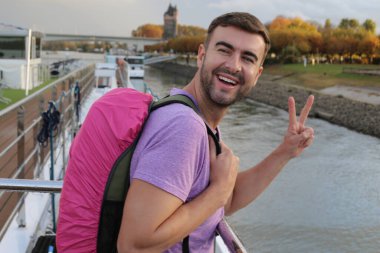 Sırt çantasıyla seyahat ederken barış jesti yapan yakışıklı bir gencin portresi