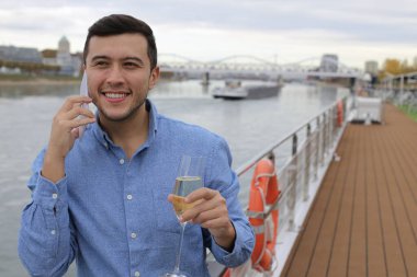 Bir bardak şampanyayla güvertede telefonla konuşan yakışıklı genç adamın portresi.