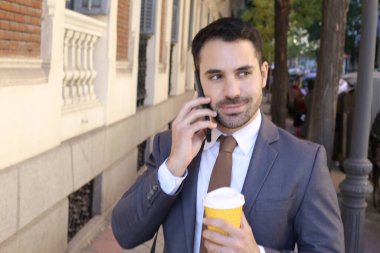 Takım elbiseli yakışıklı bir gencin portresi. Şehir caddesinde elinde bir fincan kağıt kahve tutuyor.