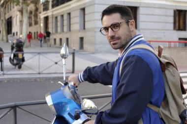 Şehir caddesinde klasik scooterlı yakışıklı bir gencin portresi.