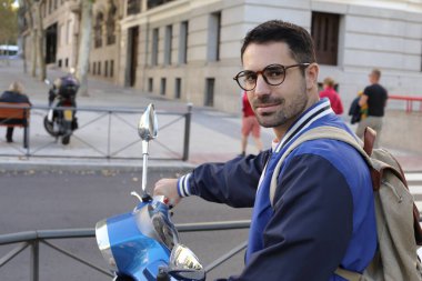 Şehir caddesinde klasik scooterlı yakışıklı bir gencin portresi.
