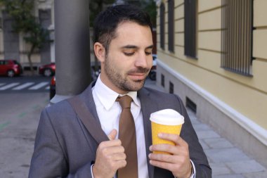 Takım elbiseli yakışıklı bir gencin portresi. Şehir caddesinde elinde bir fincan kağıt kahve tutuyor.