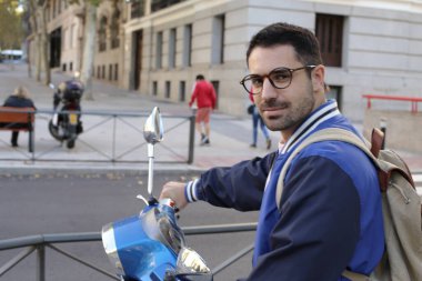 Şehir caddesinde klasik scooterlı yakışıklı bir gencin portresi.