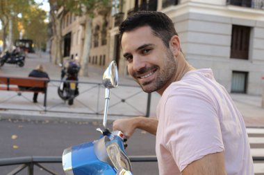 Şehir caddesinde klasik scooterlı yakışıklı bir gencin portresi.