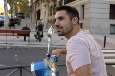 Şehir caddesinde klasik scooterlı yakışıklı bir gencin portresi.