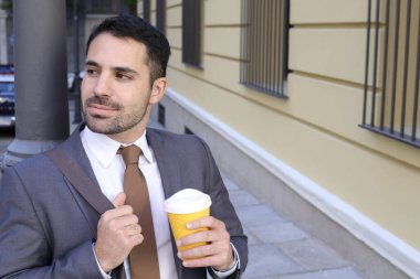 Takım elbiseli yakışıklı bir gencin portresi. Şehir caddesinde elinde bir fincan kağıt kahve tutuyor.
