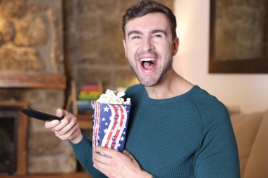 Evinde patlamış mısır ve televizyon kumandası tutan yakışıklı bir gencin yakın plan portresi.