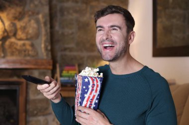 Evinde patlamış mısır ve televizyon kumandası tutan yakışıklı bir gencin yakın plan portresi.