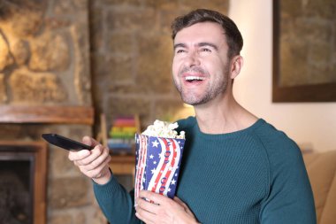 Evinde patlamış mısır ve televizyon kumandası tutan yakışıklı bir gencin yakın plan portresi.