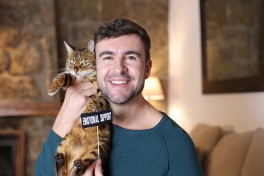 Evinde egzotik kedisini ve duygusal destek levhasını tutan yakışıklı genç adamın yakın plan portresi.