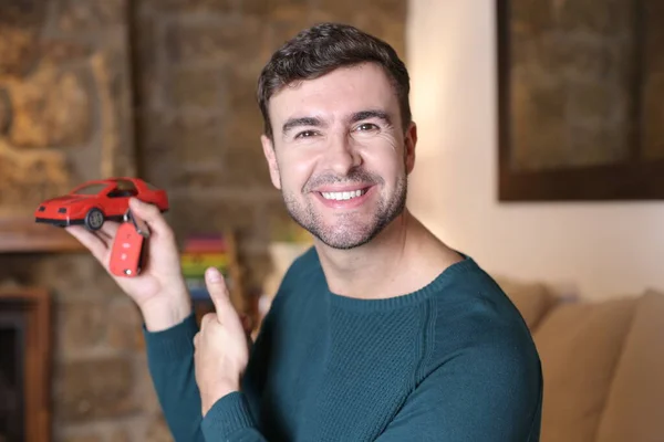 自宅で赤いおもちゃの車を持っているハンサムな若い男のクローズアップポートレート — ストック写真