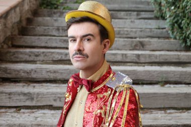 Parktaki merdivenlerin önünde renkli bir sirk elbisesi içinde yakışıklı bir genç portresi.