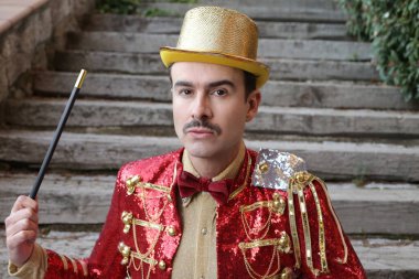Parktaki merdivenlerin önünde sihirli değnekle renkli sirk kıyafetli yakışıklı genç adamın yakın plan portresi.