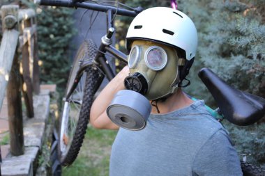 portrait of handsome young man with helmet, gas mask and bicycle on nature