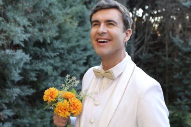 Kapıda çiçek buketi tutan şık beyaz takım elbiseli yakışıklı genç adamın yakın plan portresi.