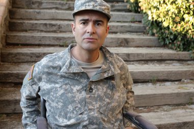 Parktaki merdivenlerin önünde tekerlekli sandalyede oturan üniformalı yakışıklı genç askerin yakın plan portresi.