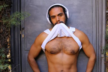 Kulaklıklı yakışıklı genç adamın yakın plan portresi gri duvar arkasında beyaz gömleğini çıkarıyor.