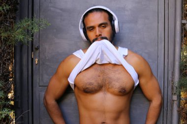 Kulaklıklı yakışıklı genç adamın yakın plan portresi gri duvar arkasında beyaz gömleğini çıkarıyor.