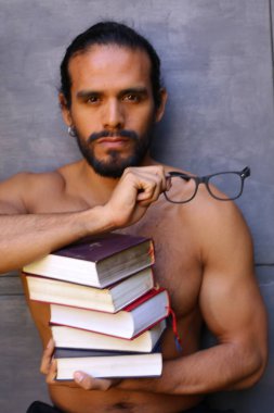 Yakışıklı üstsüz genç adamın yakın plan portresi. Arka planda gri kitap yığını var.