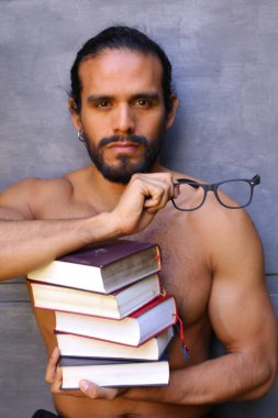 Yakışıklı üstsüz genç adamın yakın plan portresi. Arka planda gri kitap yığını var.