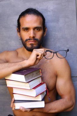 Yakışıklı üstsüz genç adamın yakın plan portresi. Arka planda gri kitap yığını var.