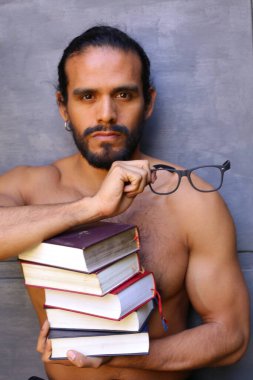 Yakışıklı üstsüz genç adamın yakın plan portresi. Arka planda gri kitap yığını var.