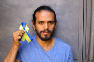 Gri duvar arkasında Ukrayna bayrağı renginde kurdele tutan yakışıklı genç adamın yakın plan portresi.