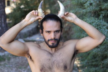 Açık havada boynuzları olan yakışıklı, üstsüz genç adamın yakın plan portresi.