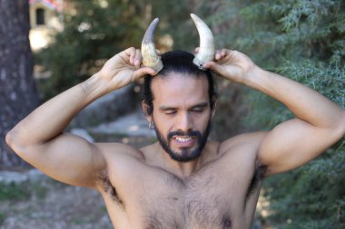Açık havada boynuzları olan yakışıklı, üstsüz genç adamın yakın plan portresi.