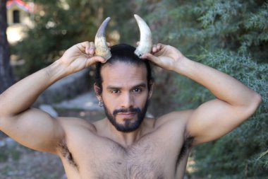 Açık havada boynuzları olan yakışıklı, üstsüz genç adamın yakın plan portresi.