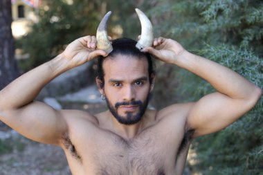 Açık havada boynuzları olan yakışıklı, üstsüz genç adamın yakın plan portresi.