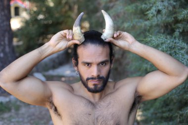Açık havada boynuzları olan yakışıklı, üstsüz genç adamın yakın plan portresi.