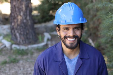 Mavi iş elbisesi ve kask giymiş yakışıklı bir genç adamın yakın plan portresi.