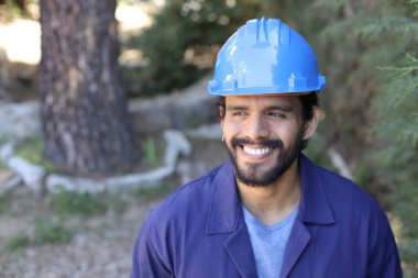 Mavi iş elbisesi ve kask giymiş yakışıklı bir genç adamın yakın plan portresi.