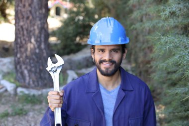 Açık havada ingiliz anahtarı takan yakışıklı bir tesisatçı portresi.