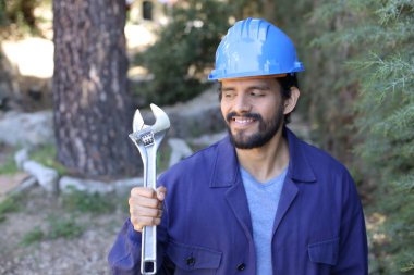 Açık havada ingiliz anahtarı takan yakışıklı bir tesisatçı portresi.