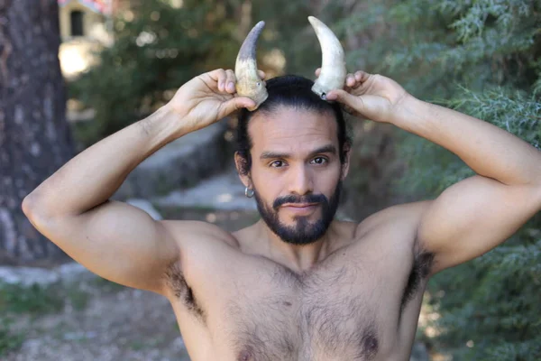 Açık havada boynuzları olan yakışıklı, üstsüz genç adamın yakın plan portresi.