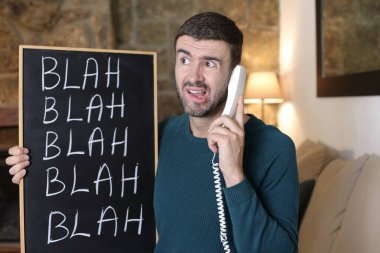 close-up portrait of handsome young man holding chalkboard with blah blah blah at home