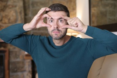 Evdeki parmaklarıyla gözlerini açan yakışıklı bir gencin yakın plan portresi.