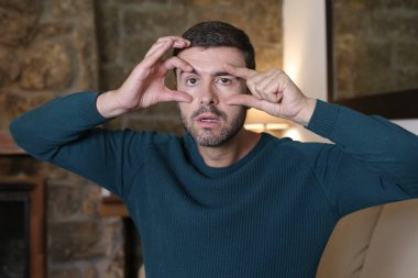 Evdeki parmaklarıyla gözlerini açan yakışıklı bir gencin yakın plan portresi.