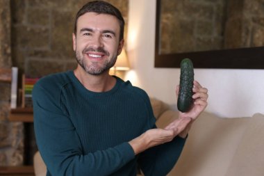 Evde olgun salatalık tutan yakışıklı genç adamın yakın plan portresi.