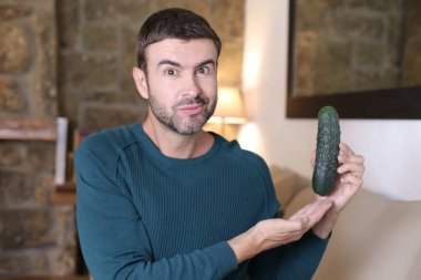 Evde olgun salatalık tutan yakışıklı genç adamın yakın plan portresi.