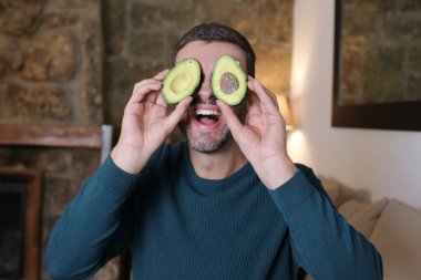 Evinde iki parça avokado tutan yakışıklı genç adamın yakın plan portresi.