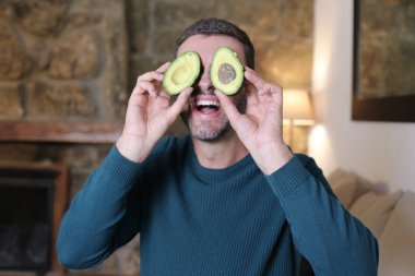 Evinde iki parça avokado tutan yakışıklı genç adamın yakın plan portresi.