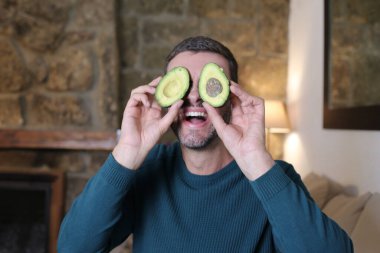 Evinde iki parça avokado tutan yakışıklı genç adamın yakın plan portresi.