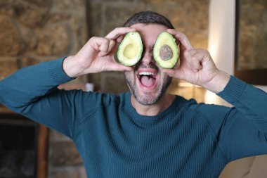 Evinde iki parça avokado tutan yakışıklı genç adamın yakın plan portresi.
