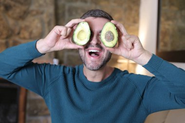 Evinde iki parça avokado tutan yakışıklı genç adamın yakın plan portresi.